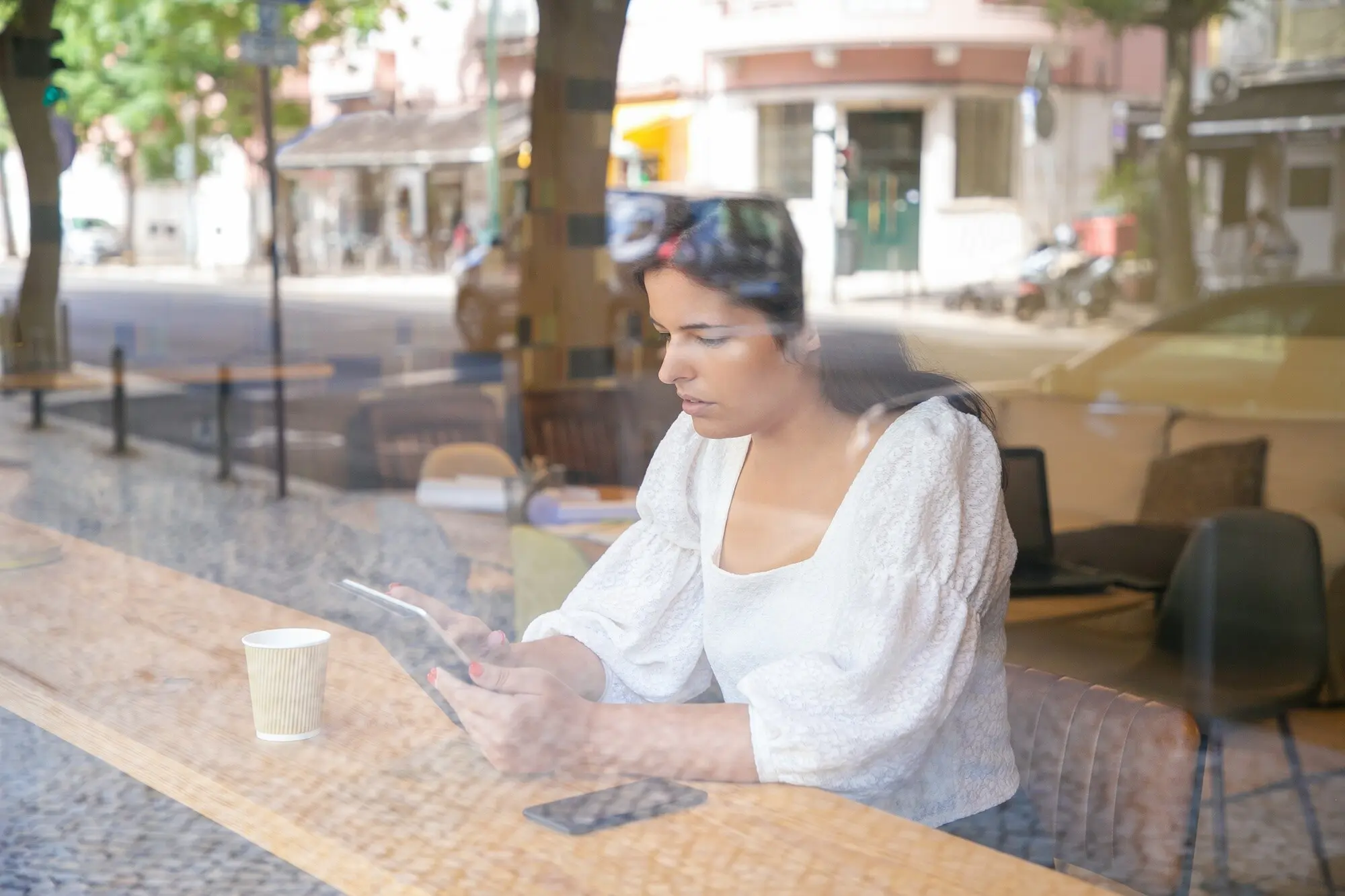 Nachdenkliche junge Geschäftsfrau sitzt an einem Schreibtisch in einem Coworking-Space oder Café und benutzt ein Tablet.